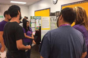 Teachers in a classroom browse between bulletin boards that display teacher-driven standards based, equitable grading policies schoolwide.