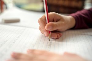 Boy writing in a notepad doing his school work such as spelling.